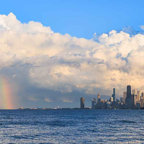 Elaborately twisted storm clouds tower the city skyline, which is set to the right of the image seemingly rising from the choppy waters of Lake Michigan. The city is lit brightly, as the dark clouds of a storm blow away to reveal a sunny day. To the left of the image, a bright rainbow shines.