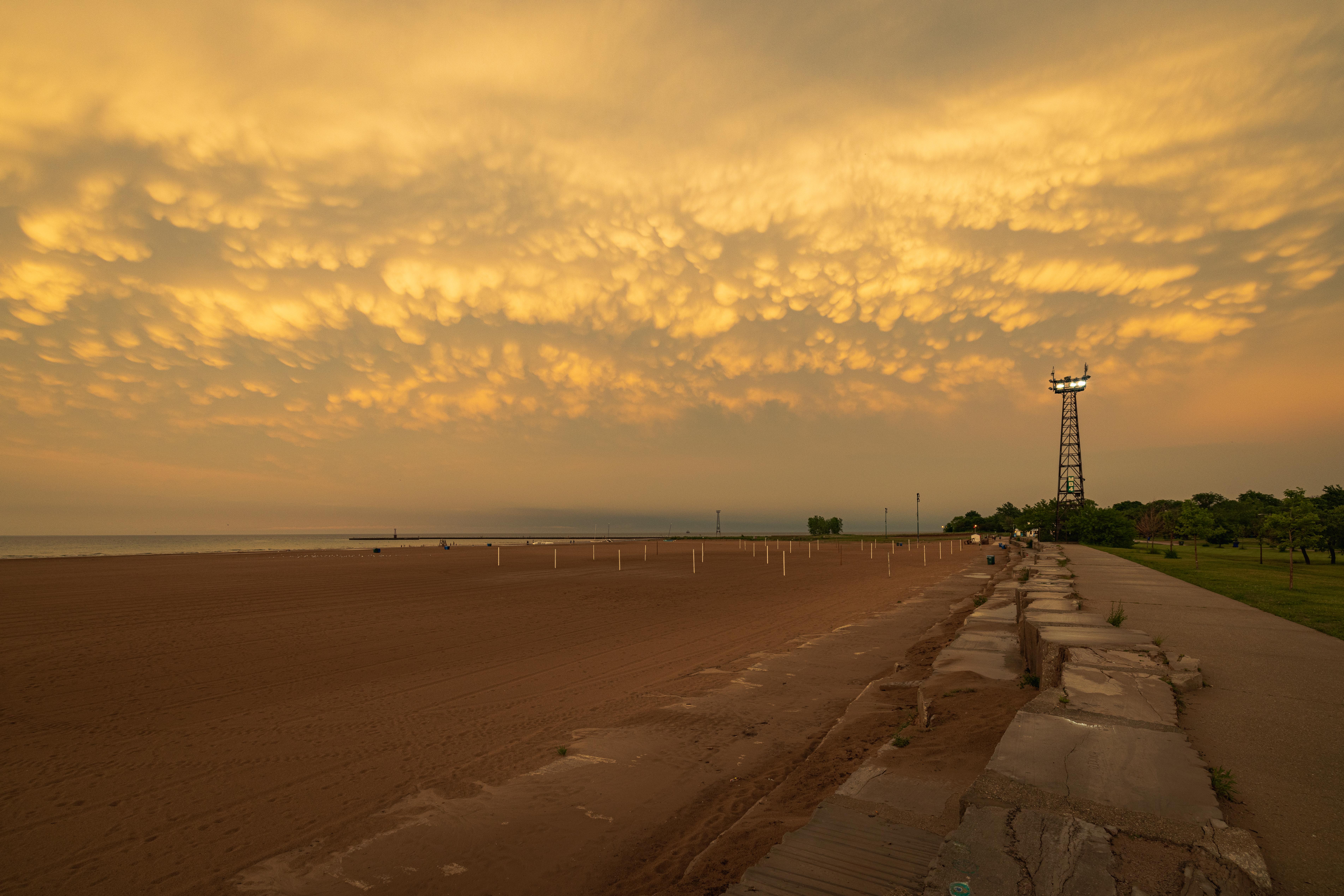 Looking down the stone wall next to the sandy Montrose beach with dramatic, fluffy clouds upset by rolling winds above