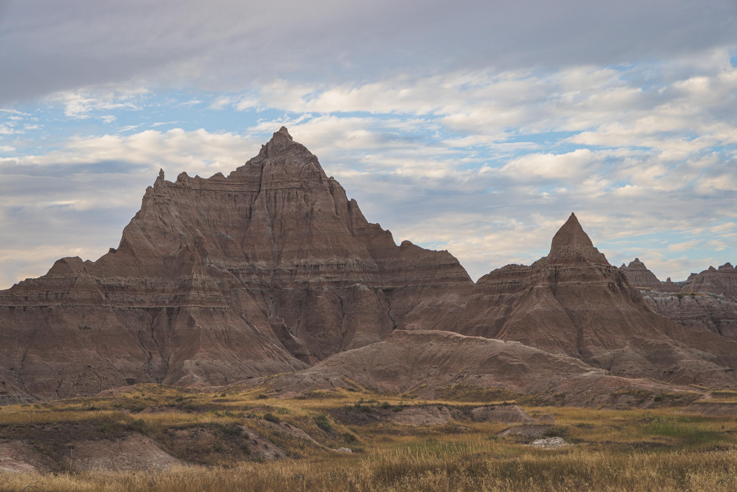 A rocky outcrop featuring reddish and grey layers of material underneath a blue sky with fluffy clouds