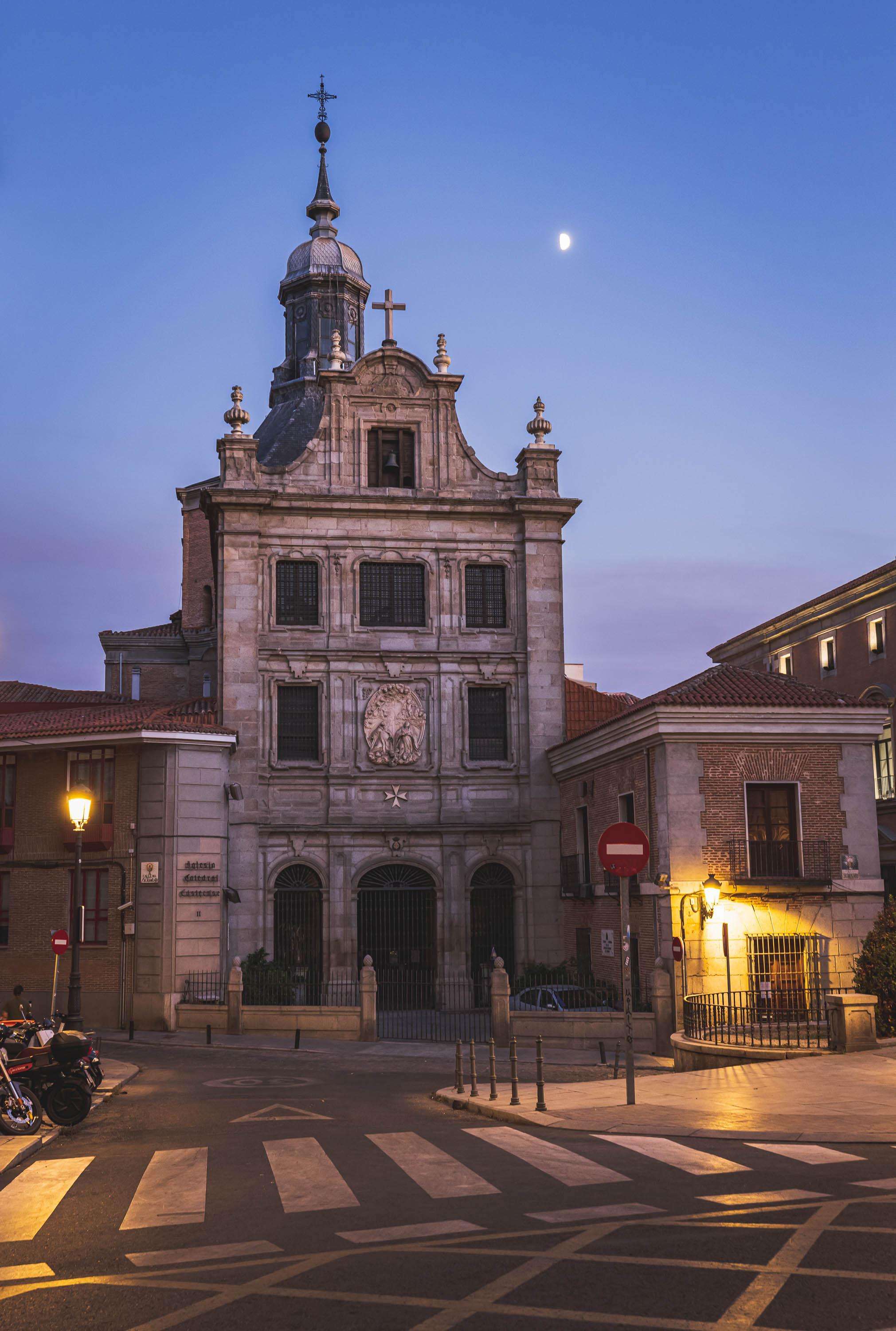 An old church seen from the street during the evening with the moon above