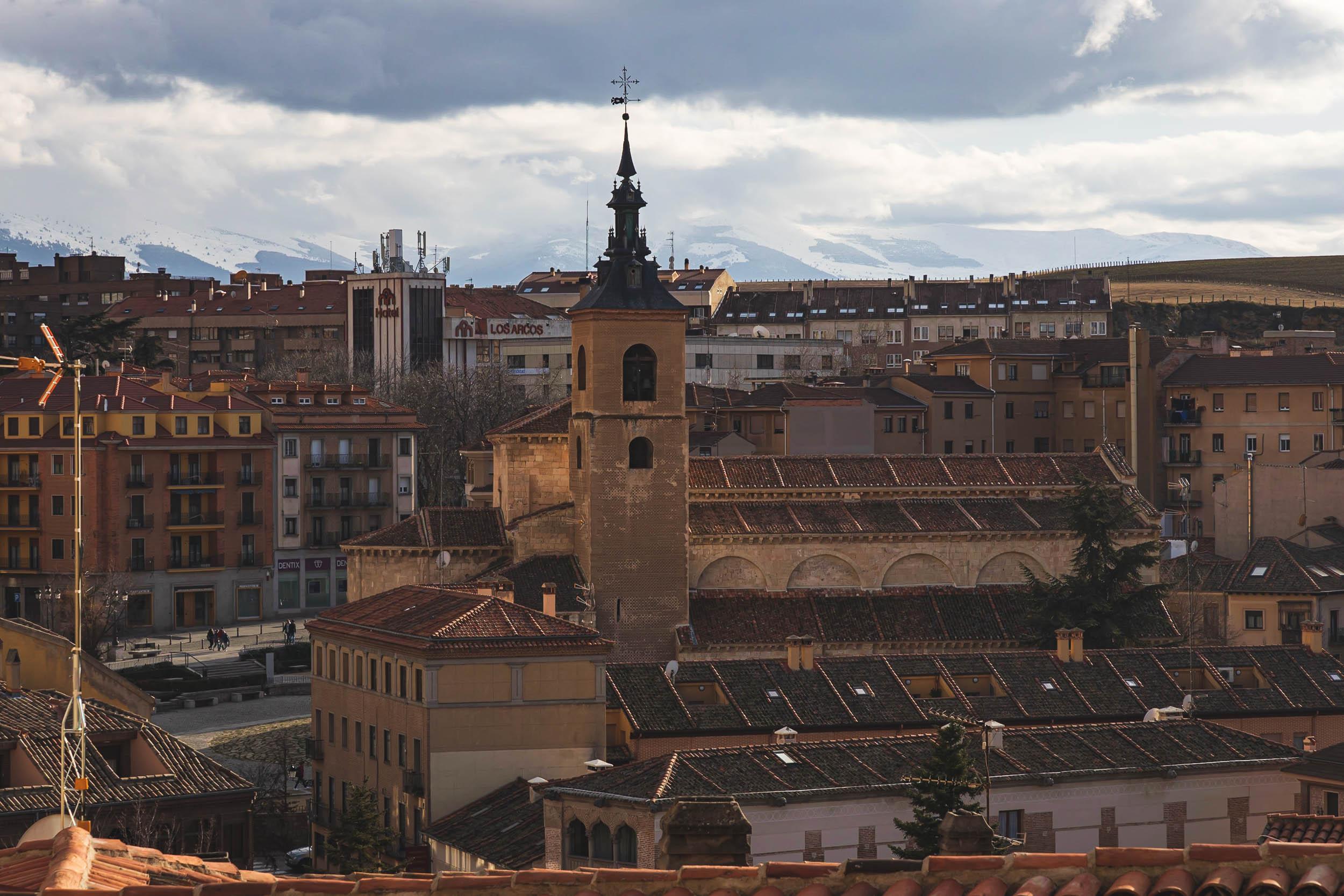 The rooftop architecture of Segovia, with snowy mountains shrouded in clouds behind