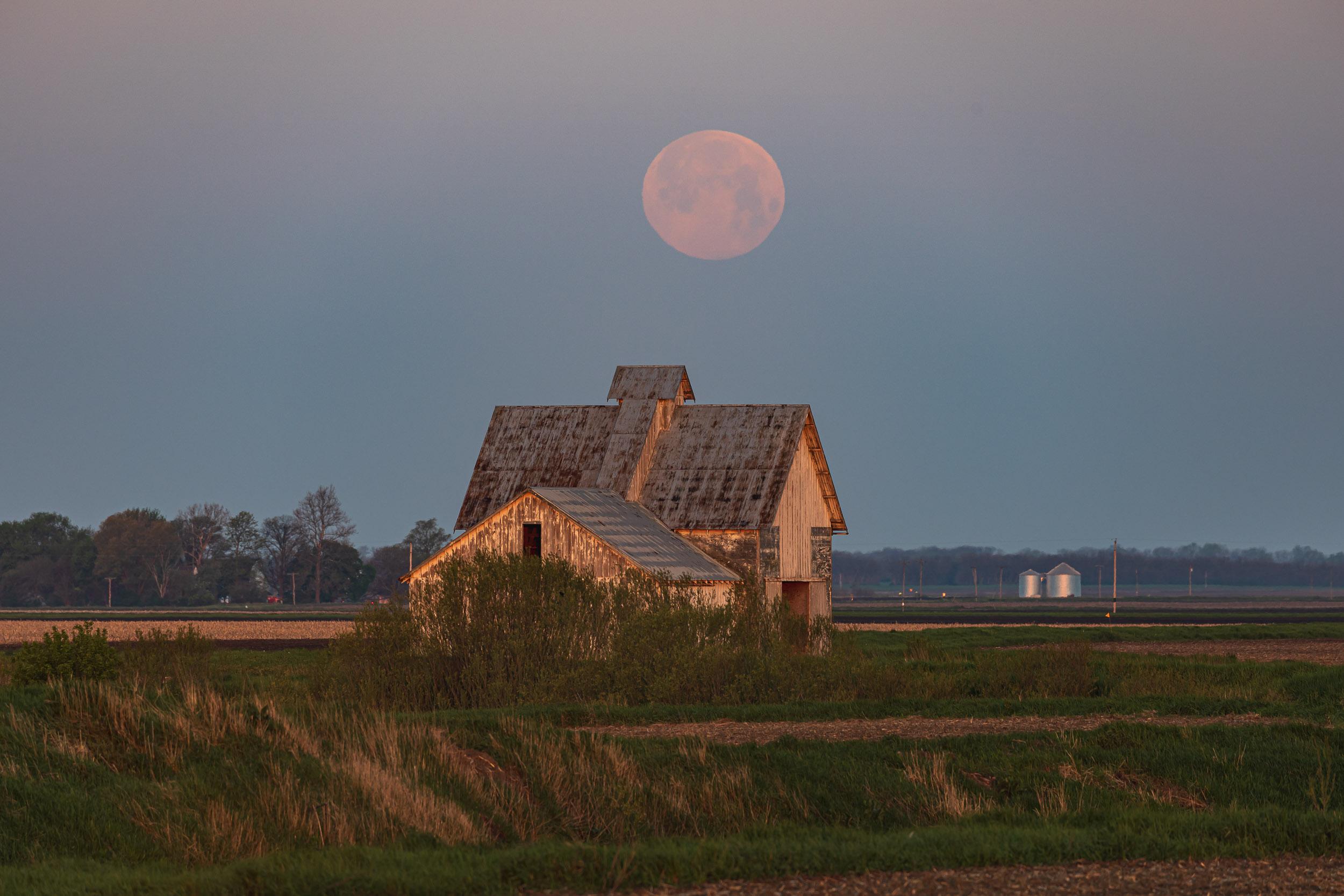 The sky becoming bright with the sunrise as the moon approaches the horizon, fading into daylight