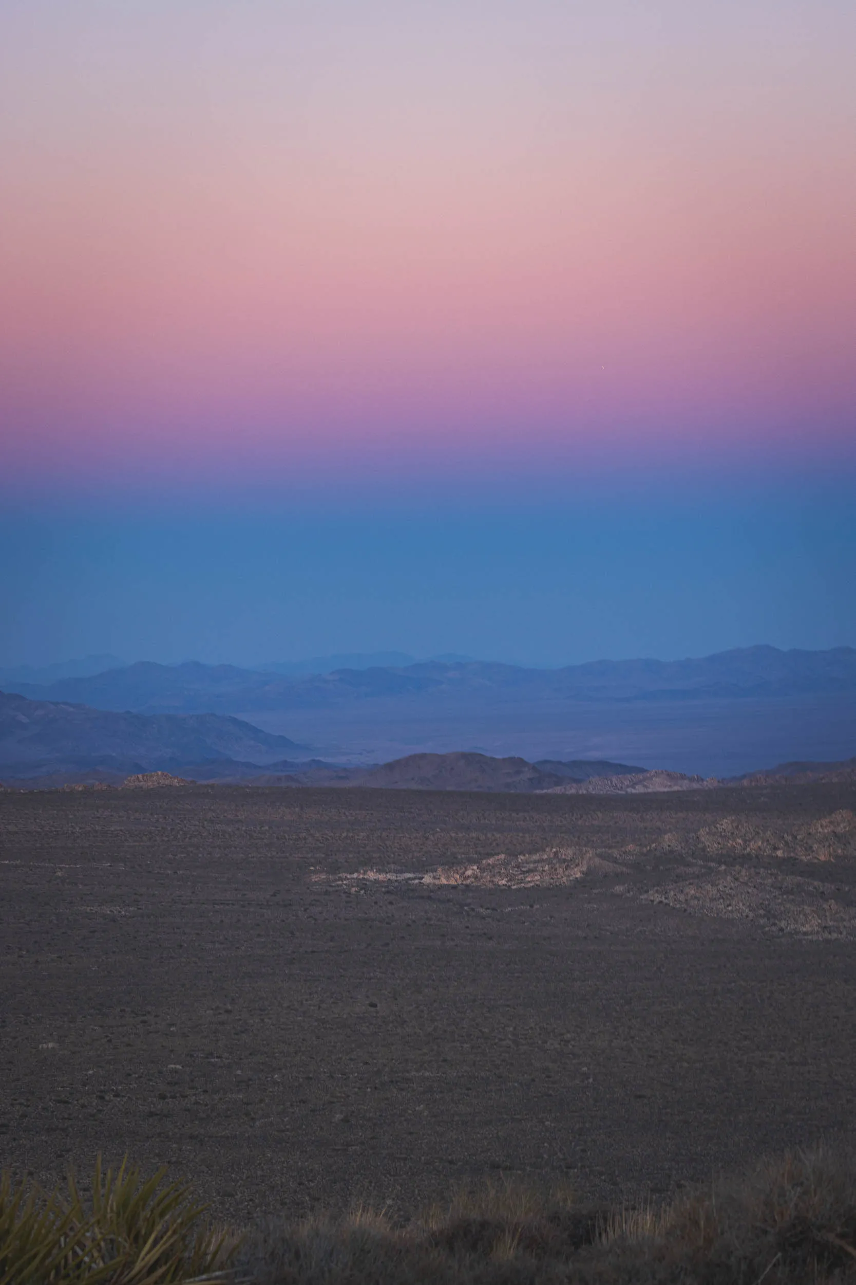 The shadow of the sunset as the sun dips below mountains in the distance