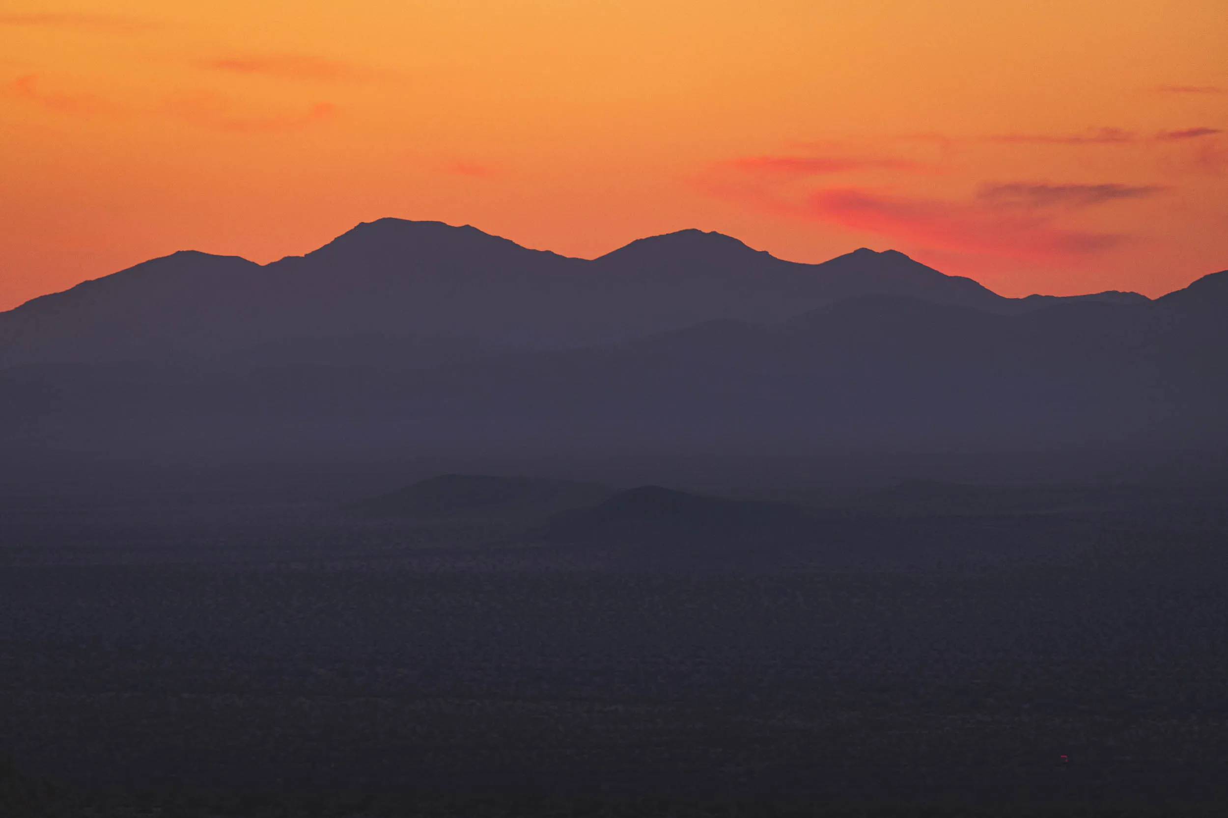 The shadow of the sunset as the sun dips below mountains in the distance