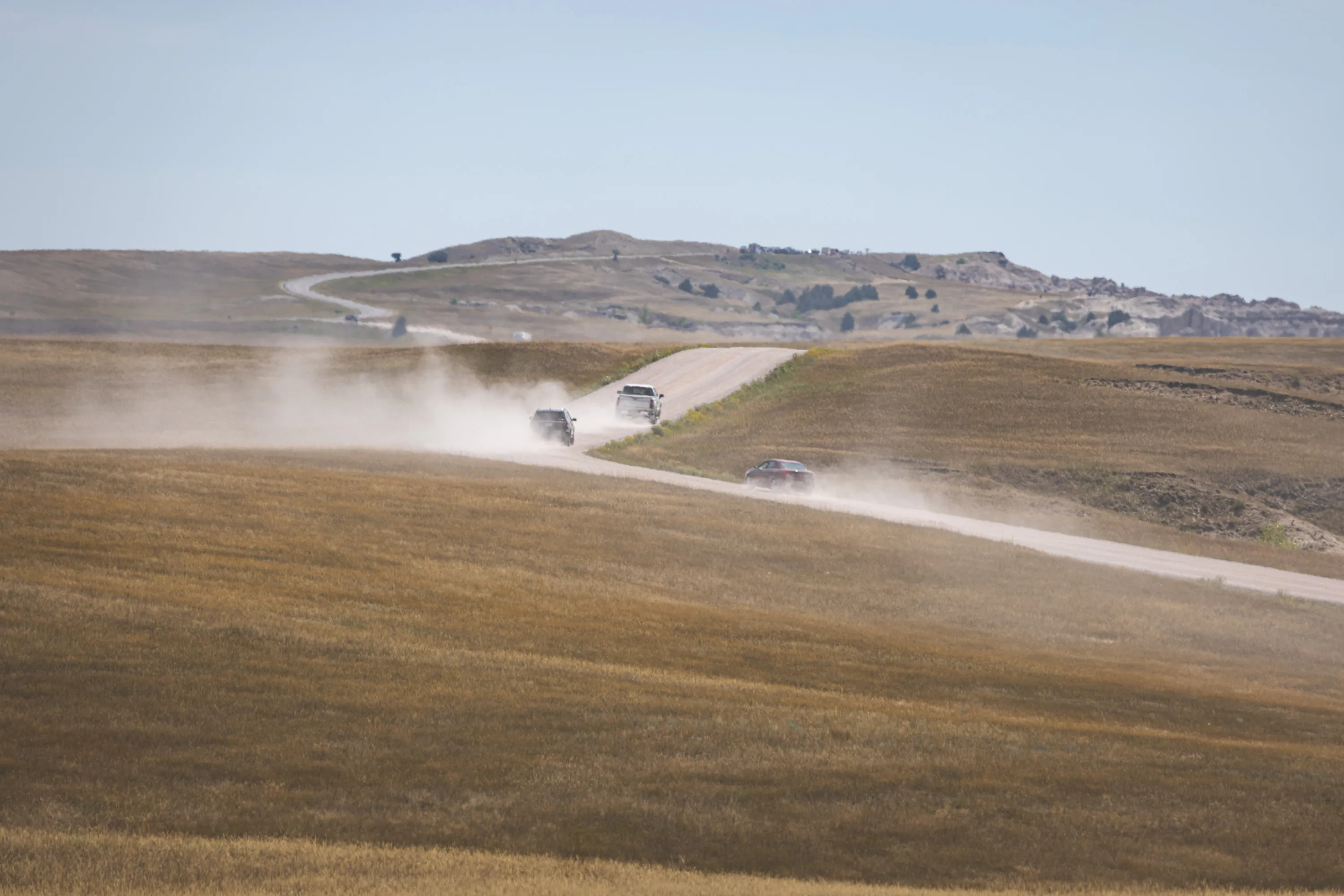 Cars in the park wind up a crushed gravel dirt road as they kick up dust clouds behind them