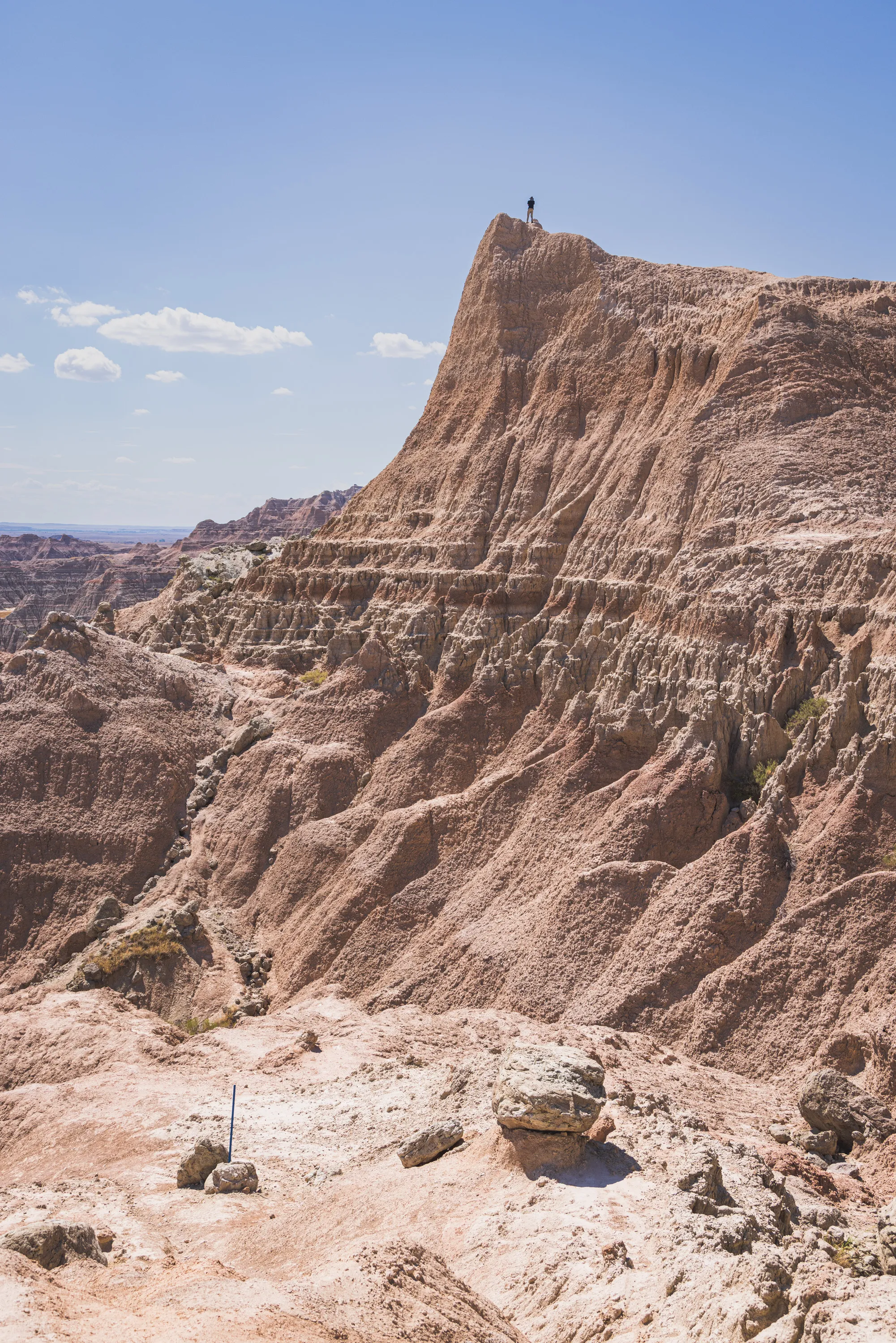 A lone figure is shown in siloutette high atop a dramatic cliff against a sunny sky, with a valley stretching out below