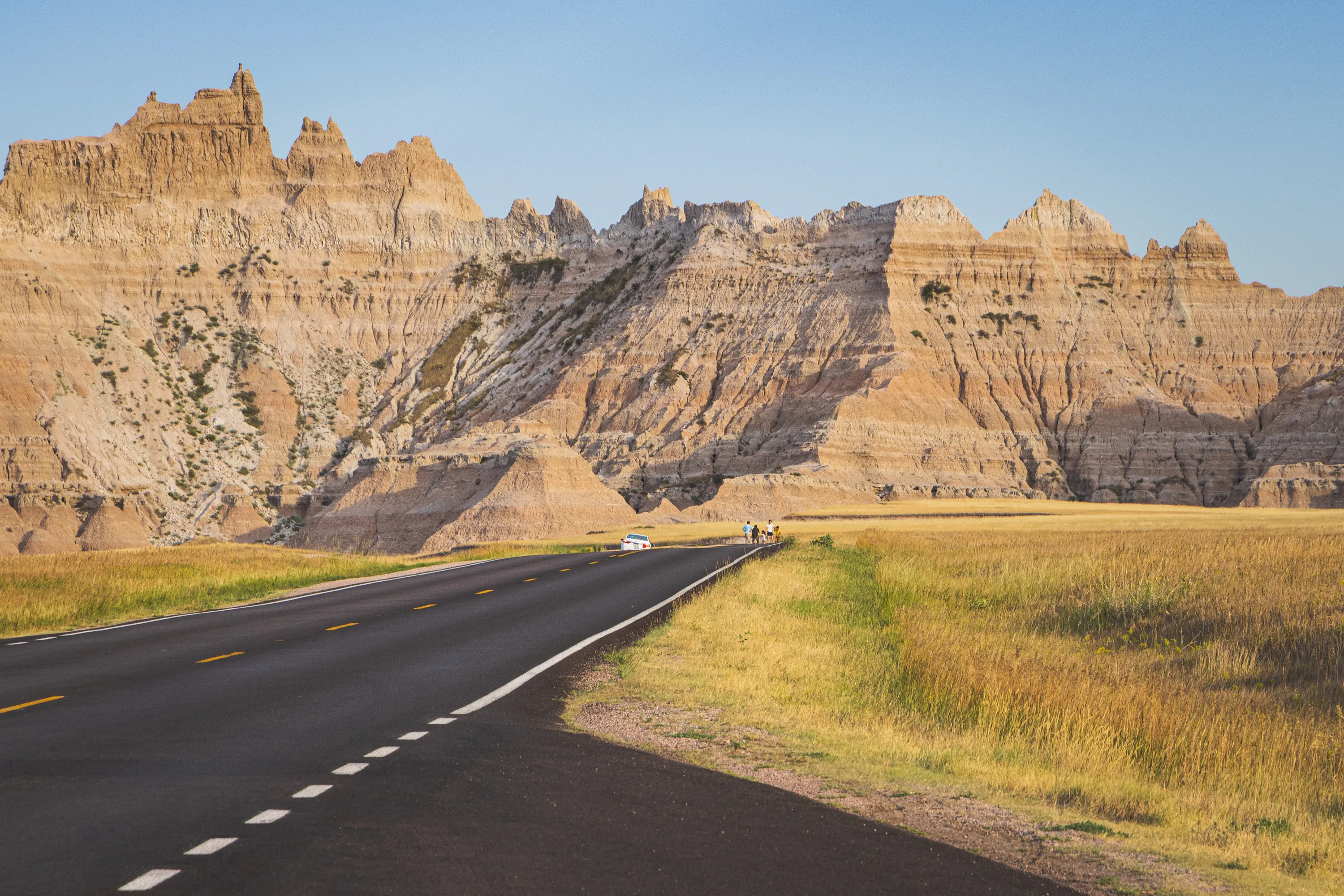 A tiny family can be seen posing for a photo in the distance, standing in the road against a backdrop of a large mountain of rocks