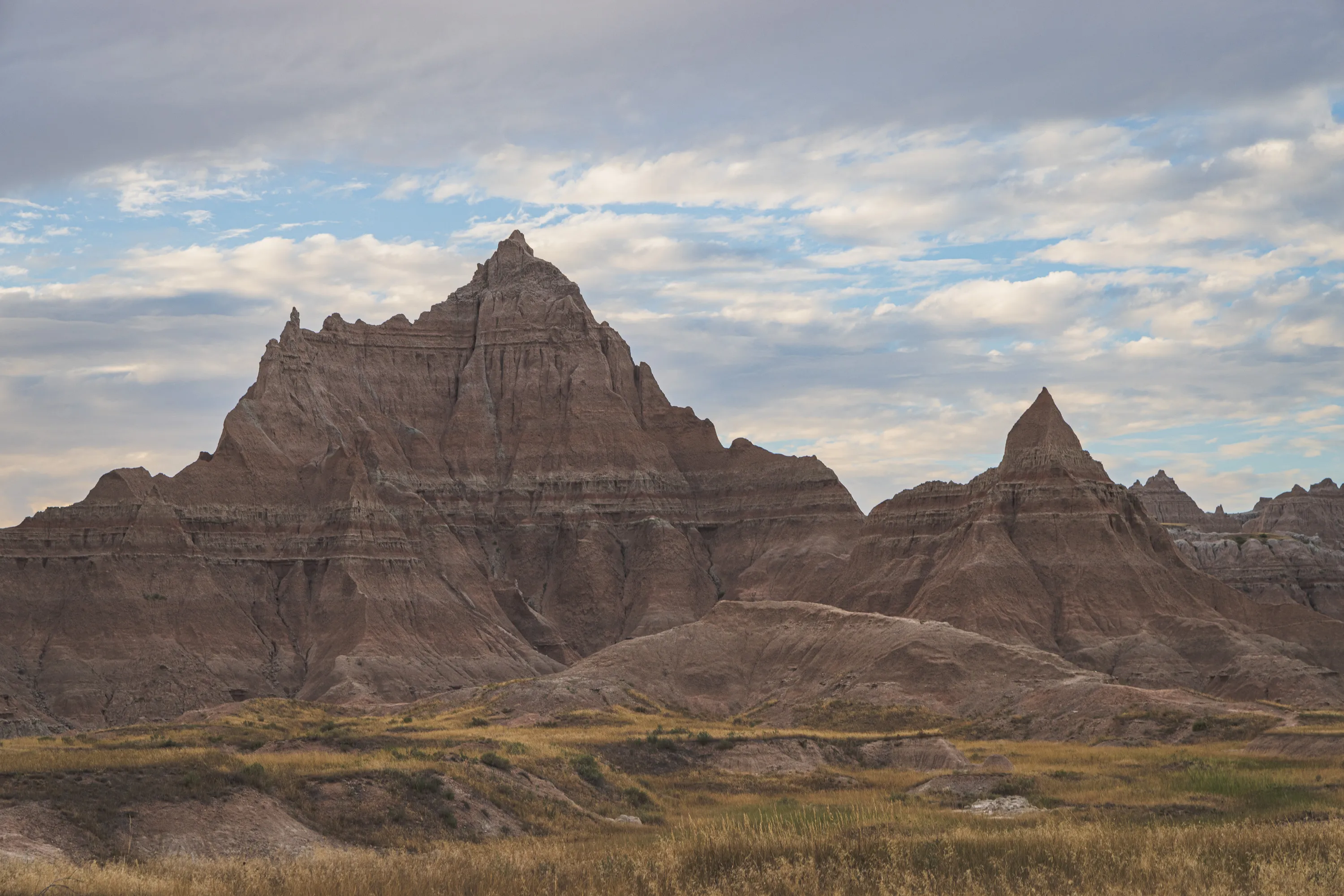 A rocky outcrop featuring reddish and grey layers of material underneath a blue sky with fluffy clouds