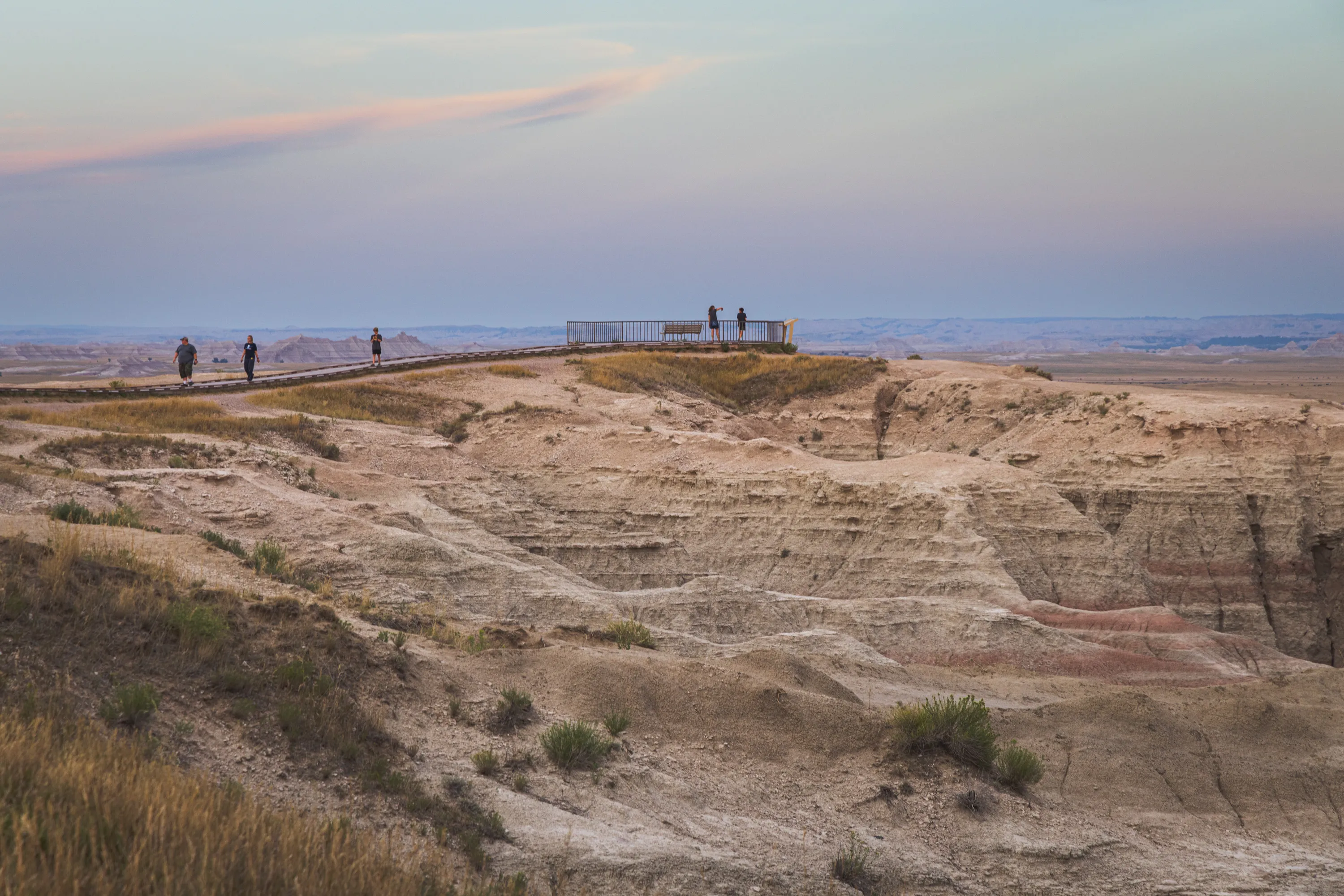 People take in a view in an observation area atop a rocky hill as others walk back on the path leading to the observation area