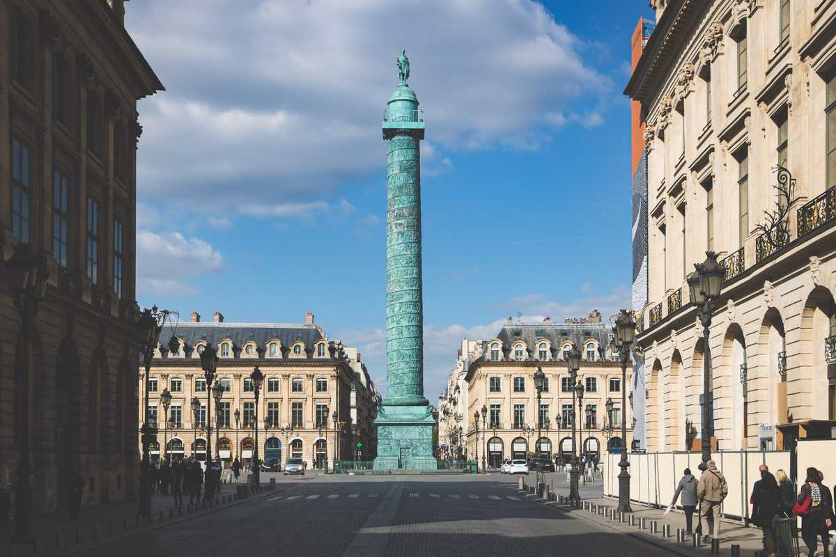 A large triumphal column turned coppery blue by the passage of time stands in the middle of a large open plaza