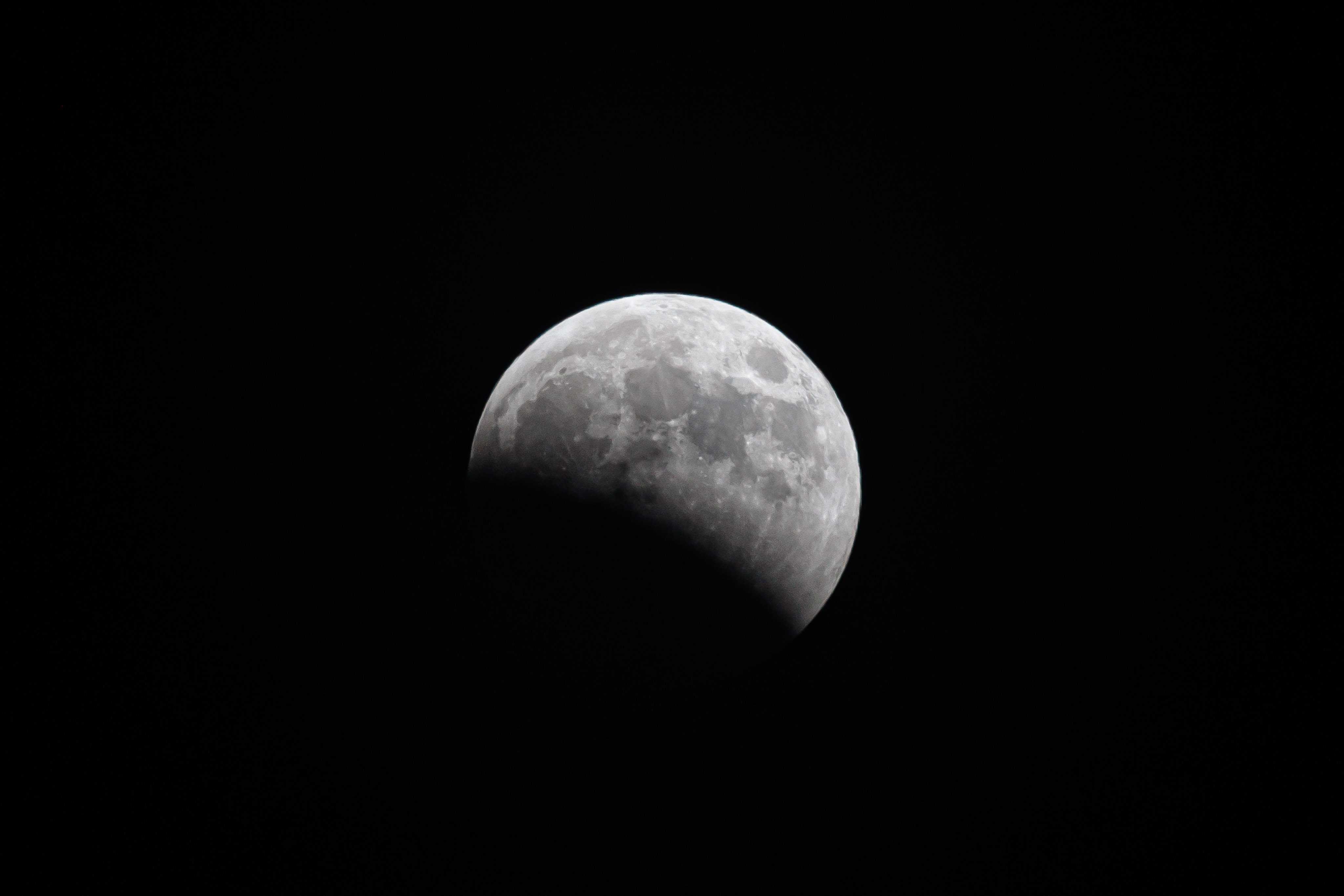 An image of the bright moon with a cookie-bite shadow cast across its lower left corner as a lunar eclipse unfolds