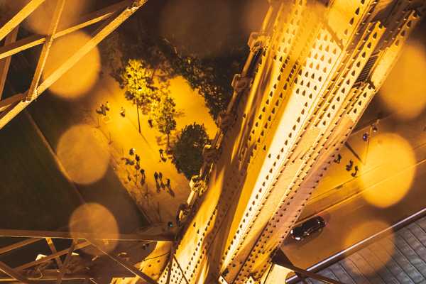 Looking down from the Eiffel Tower at the street below through cast iron beams lit by golden lights