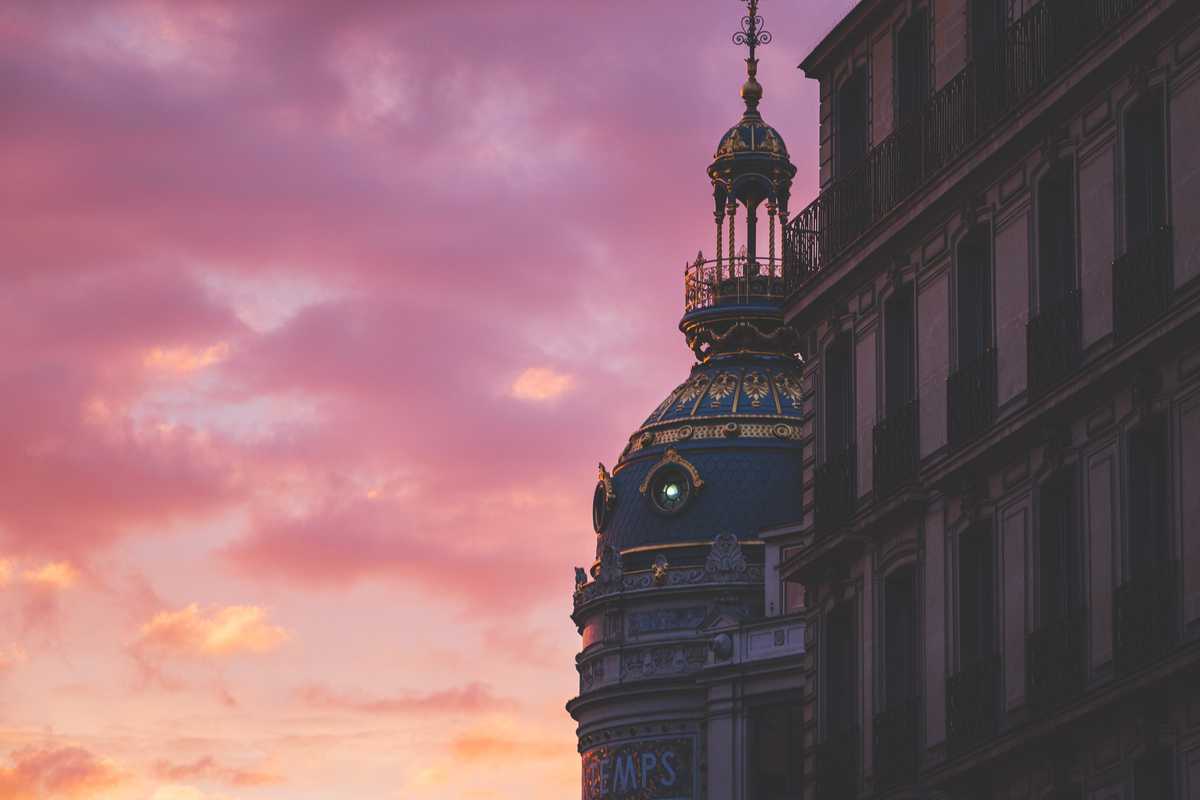 A dramatic orange and purple sunset reflects in fluffy clouds from a street in central Paris