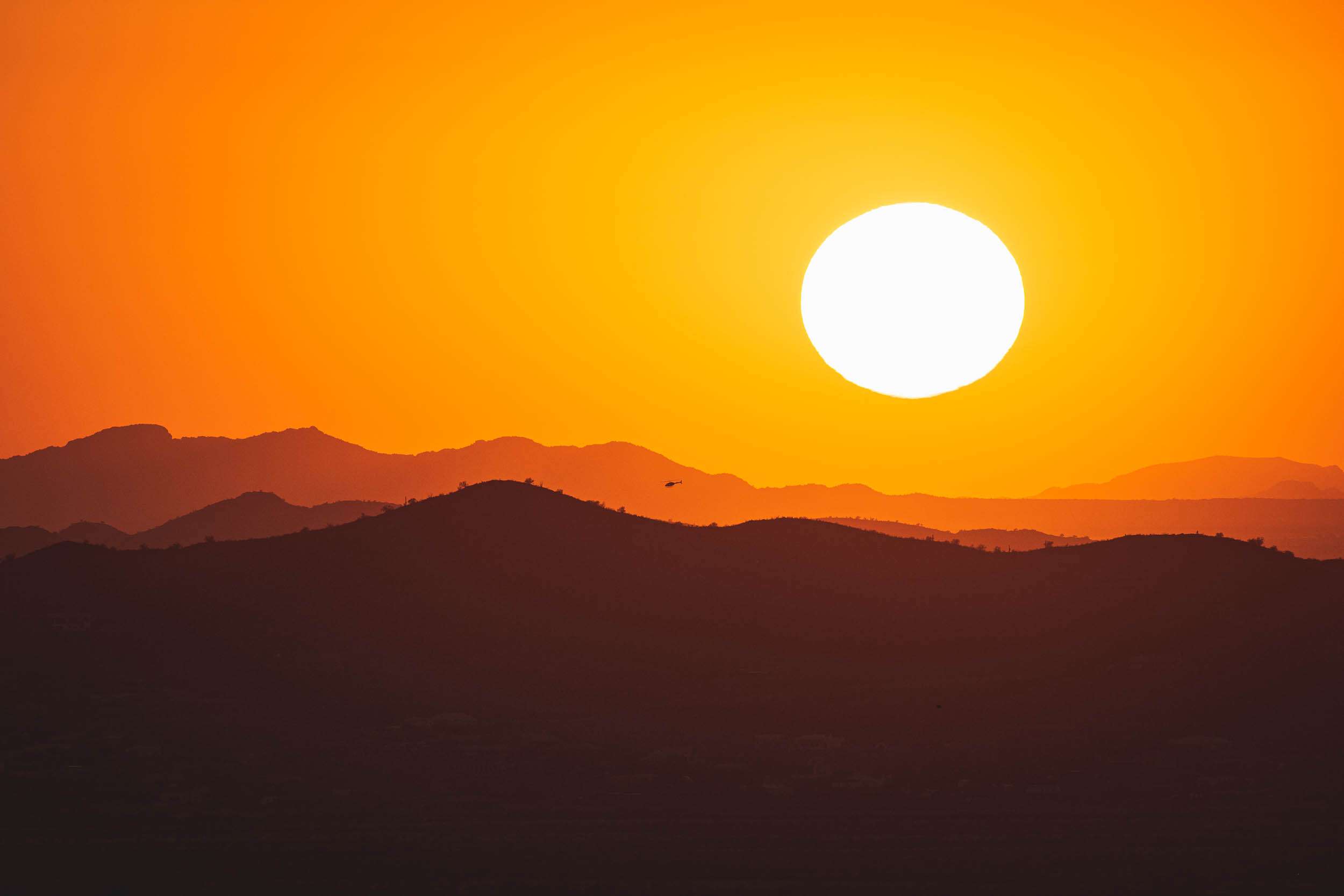 A photo of the bright yellow setting sun above layers of mountains