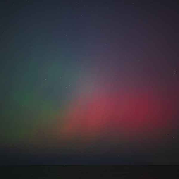 The night sky with many stars visible is glowing with green streaks on the left mixing with red streaks on the right, visible above a thin strip of Lake Michigan.