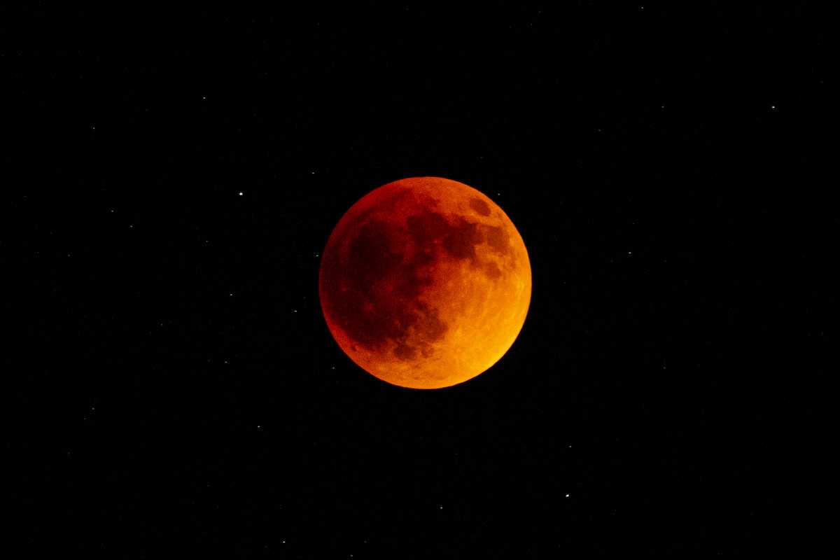 The full moon during a lunar eclipse, completely behind the earth's shadow and glowing a dull orange
