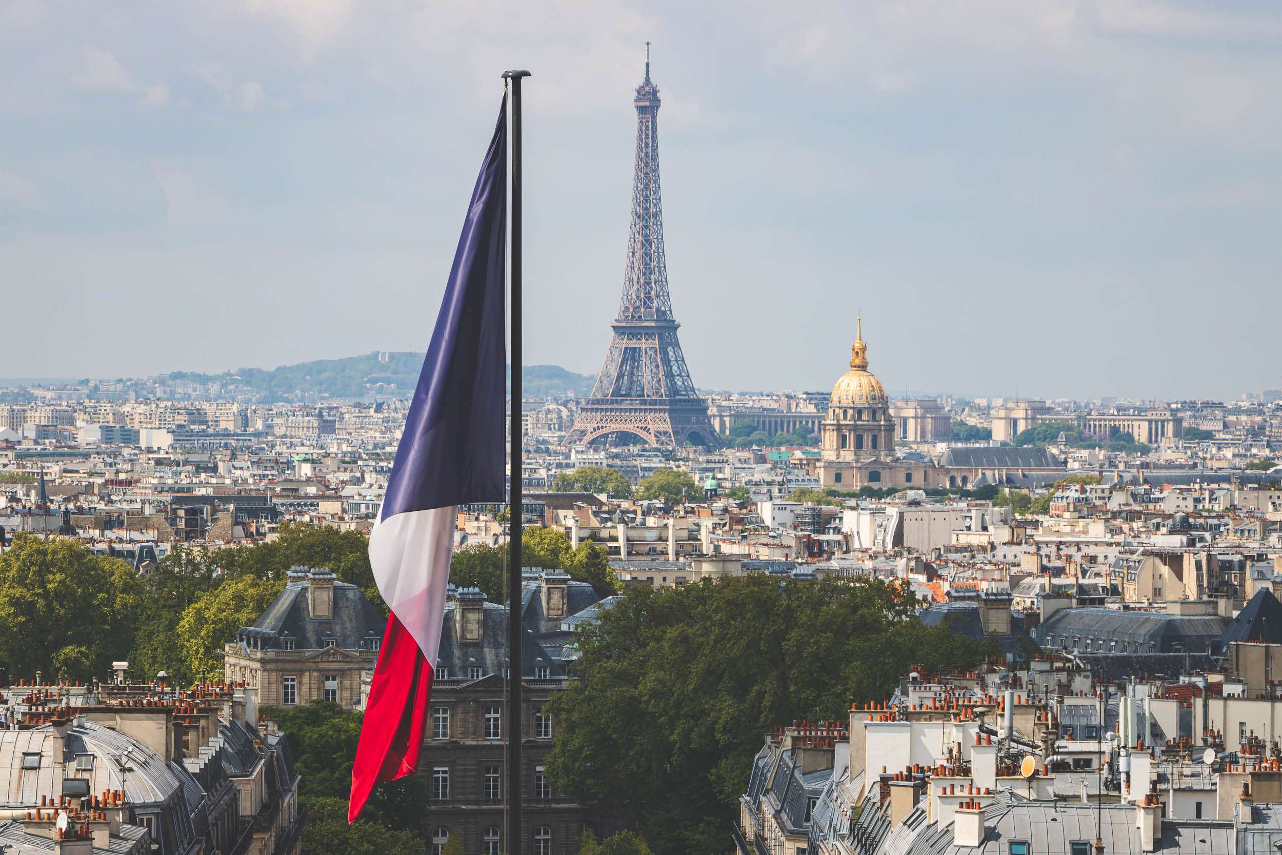 A photo of the Paris skyline from a rooftop with the French Tricolor flag standing next to the Eiffel Tower in the distance