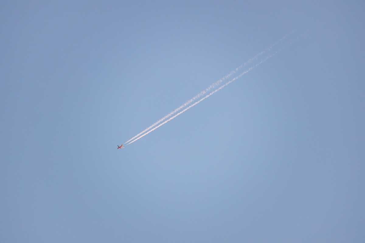 A plane flying over trailing a long whispy contrail