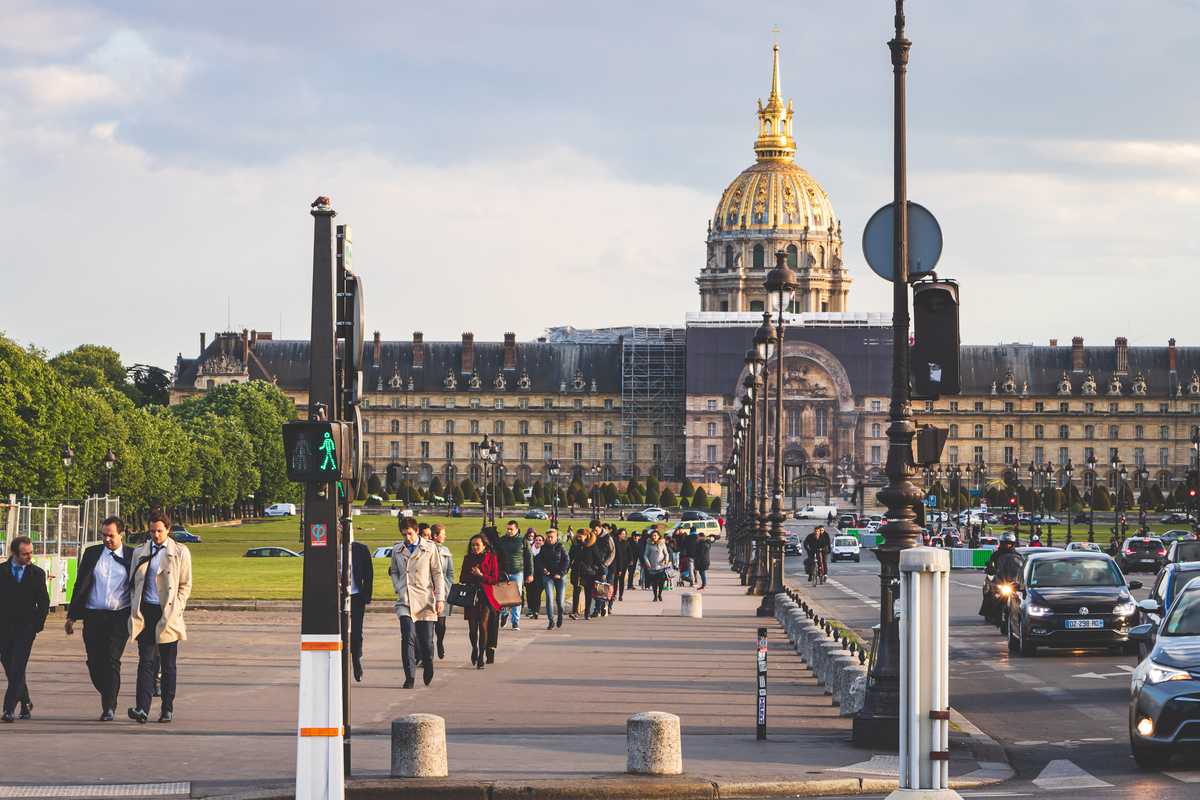 Looking down a long sidewalk filled with people, pointing straight toward Les Invalides, a large palatial building topped by a shiny golden dome