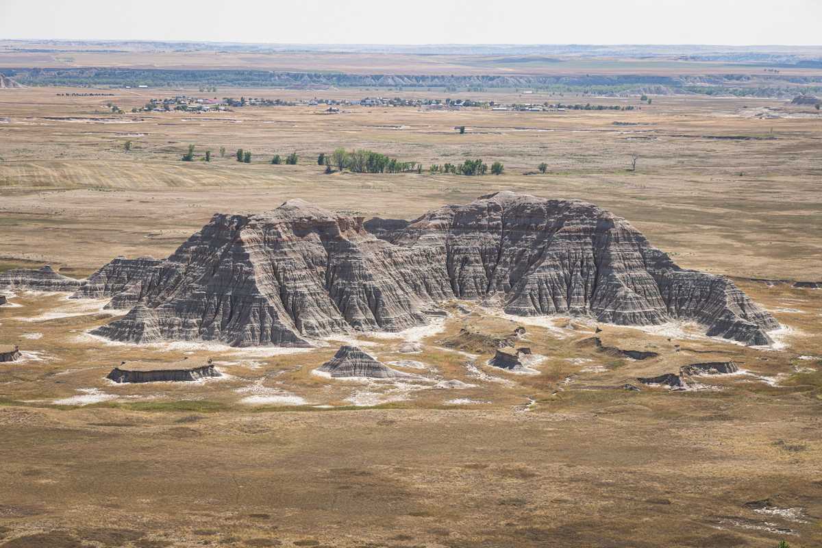 A photo showing a single mountain-like rocky outcropping rising from the grasslands, which stretch far into the distance, where a small town is visible
