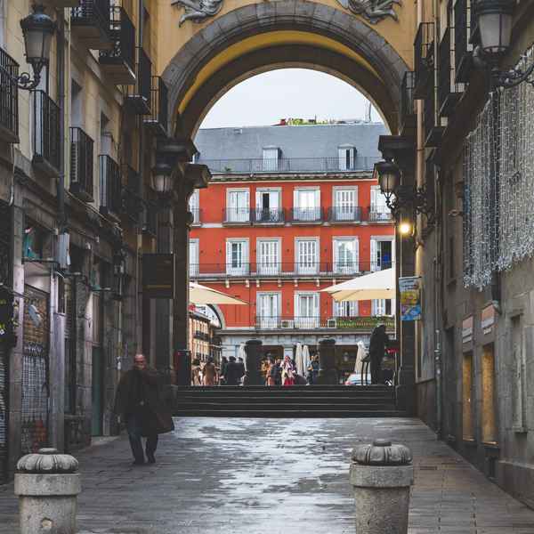 A view showing the large yellow plaster archway that opens to the bright orange painted buildings lining Plaza Mayor in central Madrid