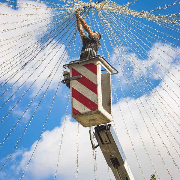 A man in a bucket lift hangs lights as they cascade down around him in a cone shape of different strings of tiny lights