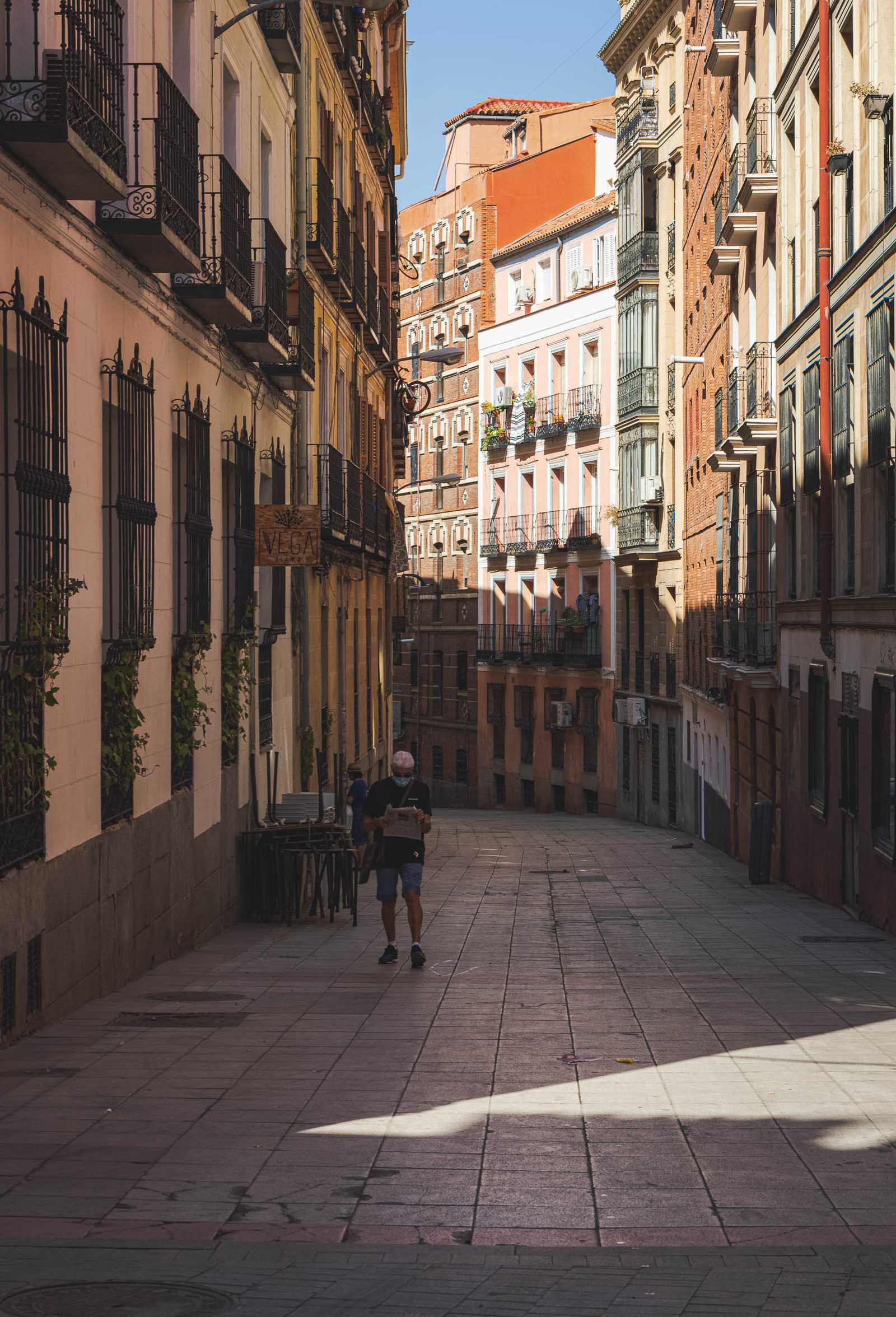 A man reading a newspaper as he steps into a narrow plaza