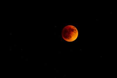 The full moon at a total eclipse shines a dull orange in the sky surrounded by stars.