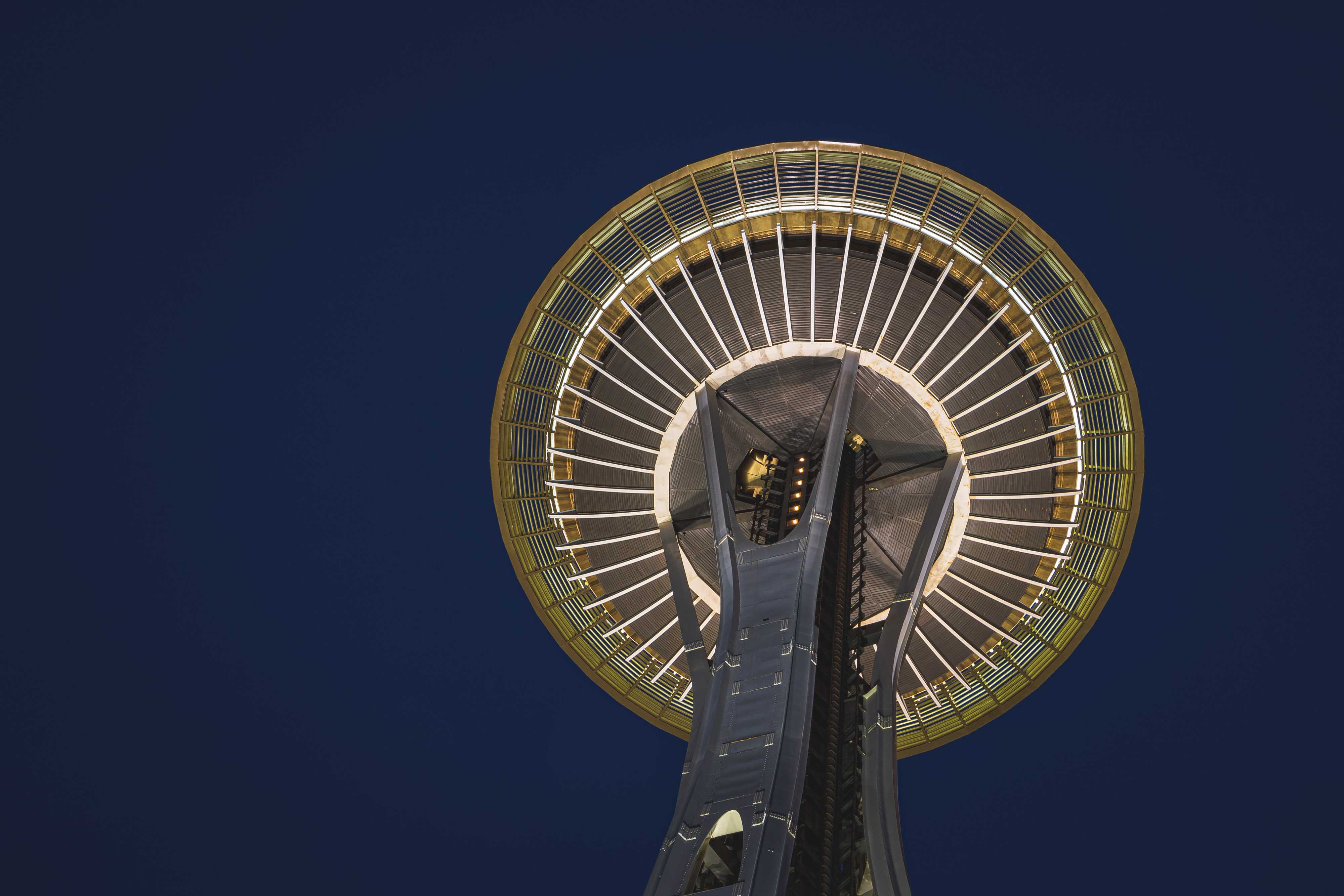 A view from underneath the Space Needle in Seattle, showing its perfectly round flying-saucer upper deck high above the air against a dark blue sky as first light breaks