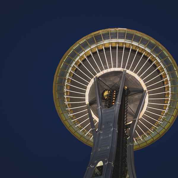 A view from underneath the Space Needle in Seattle, showing its perfectly round flying-saucer upper deck high above the air against a dark blue sky as first light breaks
