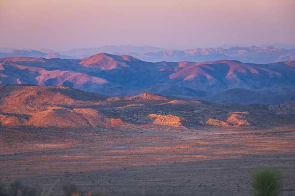 A photo of the sun setting on desert hills and mountains in Joshua Tree National Park