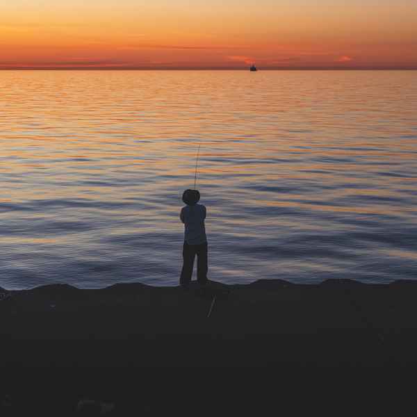 Three men fishing on the shores of Lake Michigan, their forms silhouetted against the lake gradually changing colors from blue, to yellow, to deep orange as it approaches the horizon, where the sun is rising.
