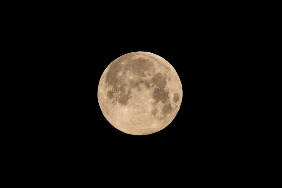 The round, full, white moon shown close up against the black of night with craters and texture visible on its surface