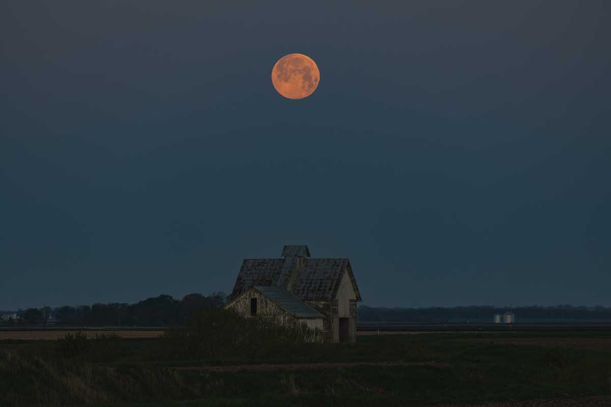Another photo: the moon sets as dawn brightens the sky above some farm buildings in a field