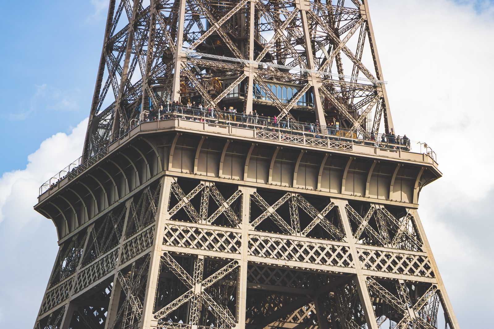 A view of one of the observation levels on the Eiffel tower, with tiny people visible among the dull grey-brown wrought iron of the archiecture