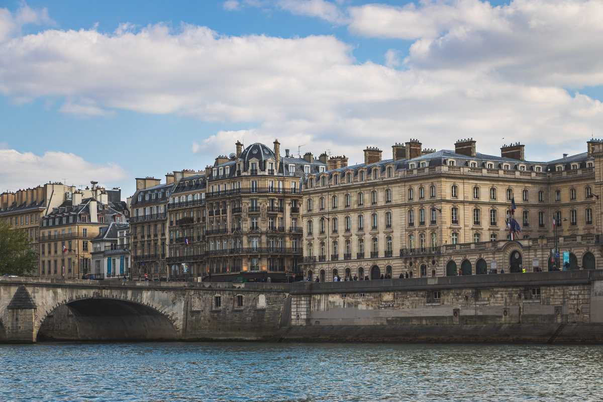 Looking across the calm River Seine at neatly arranged cream-colored stone buildings with mansard roofs in the iconic Parisian architectural style