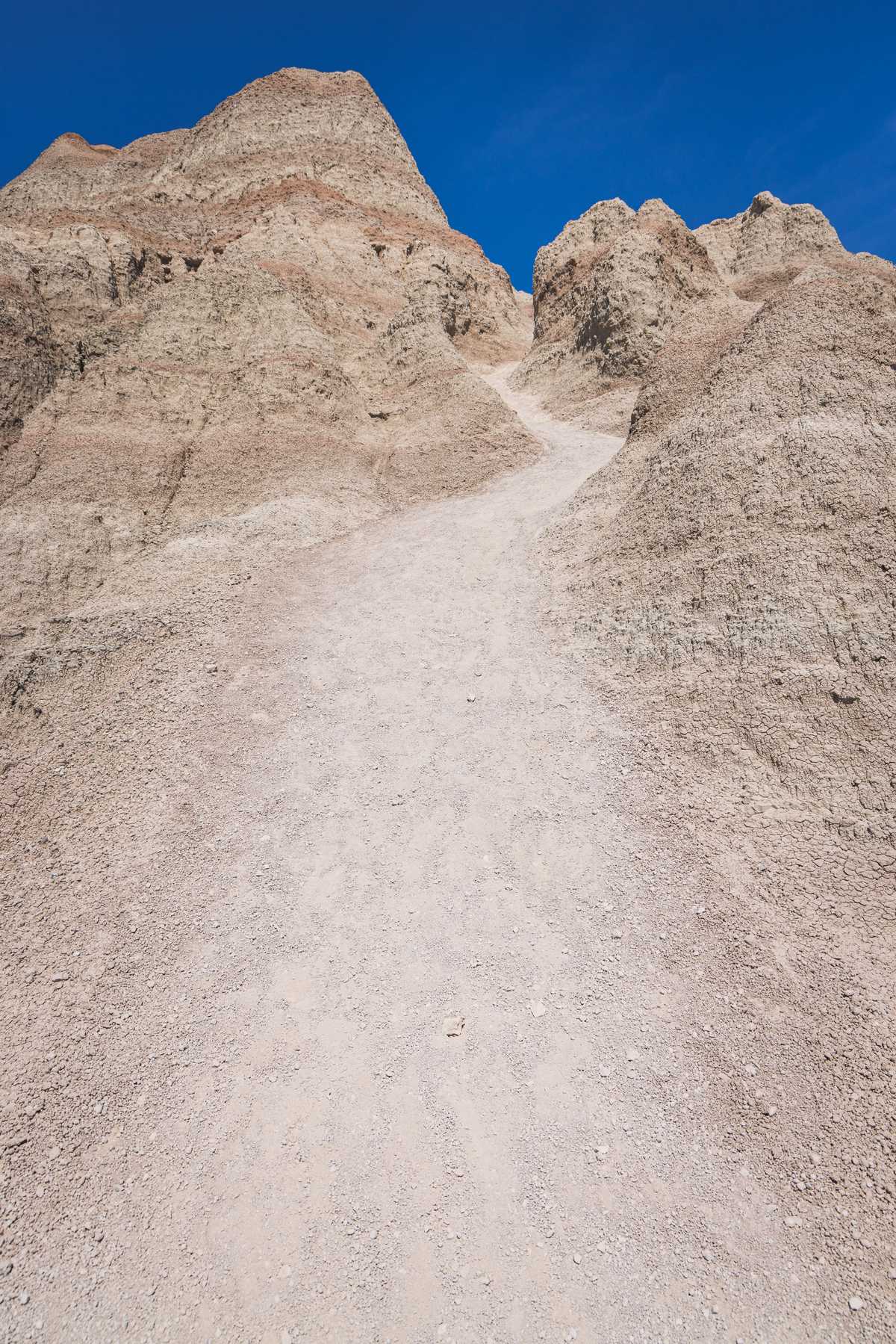 A smooth, worn path winds up a steep hill in between rough rock formations under a bright blue sky